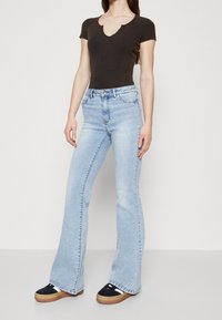 Černý žebrovaný body s krátkým rukávem a výstřihem do V, spárovaný se světle modrými zvonovými džíny a černými platformovými botami s gumovou podrážkou.