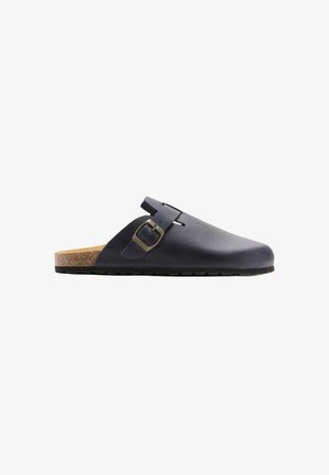 Sabot en cuir bleu marine à bout fermé, à enfiler, avec une boucle latérale réglable et un talon semelle en liège sur fond blanc.
