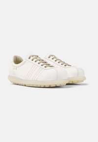 Sneaker in pelle bianca con lacci beige, caratterizzati da dettagli di design a coste e una suola spessa color crema con un motivo ruvido per la presa.