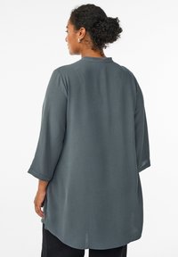 Dugih rukava, tamnosiva majica s teksturiranim materijalom, ravnog kroja i okruglog izreza, nosi se uz crne hlače.