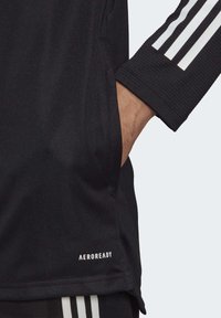 Zwarte sportshirt met geribde lange mouwen, voorzien van drie witte strepen op de mouwen en een "AEROREADY" label nabij de zoom.