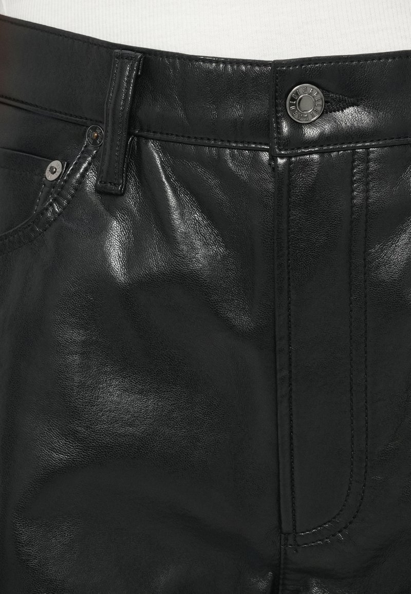 Pantaloni in pelle nera con una texture lucida, dettagli cuciti, chiusura con bottone in metallo e tasca frontale con rivetto.