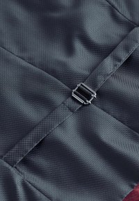 Tejido texturizado gris oscuro con un patrón hexagonal, que presenta un clip metálico y un detalle de correa suave.