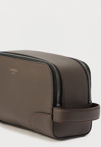 Barna bőrönd kozmetikai táska texturált felülettel, fekete cipzáras záródással, kontrasztosan varrott részletekkel és oldalsó fogantyúval a könnyű hordozáshoz.