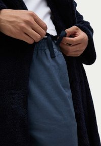 Granatowy, puszysty szlafrok z fakturowanej tkaniny, nałożony na jasnoszary t-shirt; regulowanie elastycznego pasa ciemnoniebieskich spodni z czarnym sznurkiem.