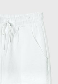 Pantalon blanc à taille élastique avec poches avant et fermeture à cordon noué, présenté sur un fond gris clair.