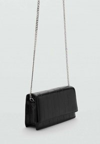 Borsa a tracolla in faux leather nera con una forma strutturata, motivo a crocodaile testurizzato e tracolla in catena argentata. Chiusura a pattina magnetica.