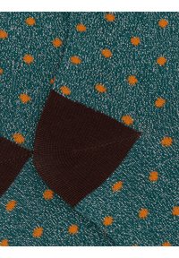 Knitted socks with a teal base and orange polka dots, accented by a brown ribbed cuff and a shimmering yarn texture.