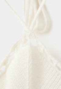 Gros plan d’un tissu blanc tricoté avec des bretelles tressées nouées en haut sur un fond uni.