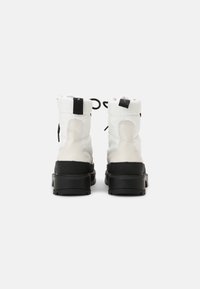 White and black ankle boots featuring a textured leather upper, round toe, thick rubber sole, and pull tabs at the back for easy wear.