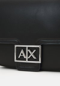 Sac à main en cuir noir avec une texture lisse, doté d'un fermoir en métal argenté avec logo. Forme structurée avec des accents de couture visibles.