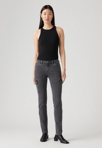 Črna brezrokavna bodi z oprijetim krojem, v kombinaciji z sivimi skinny jeans hlačami, ki imajo cargo žepe in rahlo elastičnost. Čevlji so črni usnjeni.