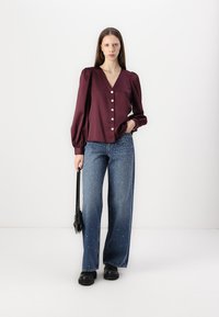 Maroon, long-sleeve blouse with a v-neck and front button closure. Paired with wide-leg, blue jeans featuring scattered white embellishments.