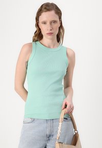 Mintgrønn ripset tanktop med rund hals, kombinert med lyseblå denimshorts og en beige håndveske med et logobånd.