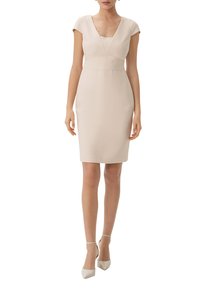 Helles, beigefarbenes, tailliertes Kleid mit V-Ausschnitt und kurzen Ärmeln. Glatter Stoff, knielang, Nähte betonen die Taille. Kombiniert mit hellen Absätzen.