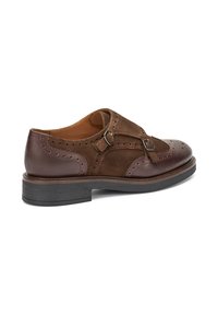 Scarpa in pelle e suede marrone con design brogue, caratterizzata da fibbie e suola testurizzata. Punta rotonda e materiali a contrasto.