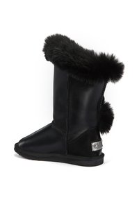 Bota de cuero negro con un trim de pelo corto en la parte superior, un pompón de pelo redondo en la parte trasera y una etiqueta metálica decorativa en el lado.