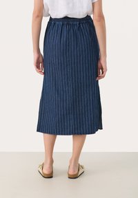 Falda midi de mezclilla en azul oscuro con rayas verticales blancas, cinturilla elástica, aberturas laterales y una textura suave. Llevada con sandalias de color claro.