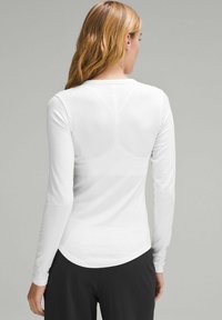 Camicia bianca a maniche lunghe con orlo arrotondato, texture a costine e forma aderente, abbinata a pantaloni scuri, che mette in mostra un design semplice.