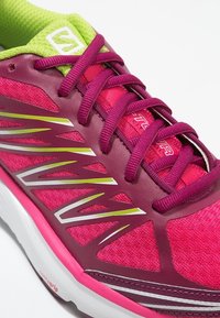 Sport sko med övre i rosa och lila tyg, med vita och limegröna detaljer, texturerade snören och en dämpad sula.