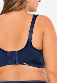Reggiseno blu navy con spalline regolabili, chiusura a gancio e occhiello, tessuto morbido e un’etichetta sul bordo; progettato per comfort e supporto.