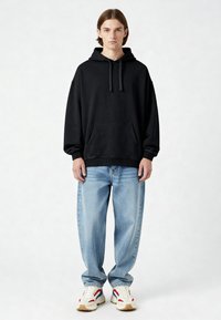 Felpa nera con cappuccio e tasca frontale, vestibilità comoda, abbinata a jeans baggy blu chiaro e sneakers multicolori con una suola testurizzata.