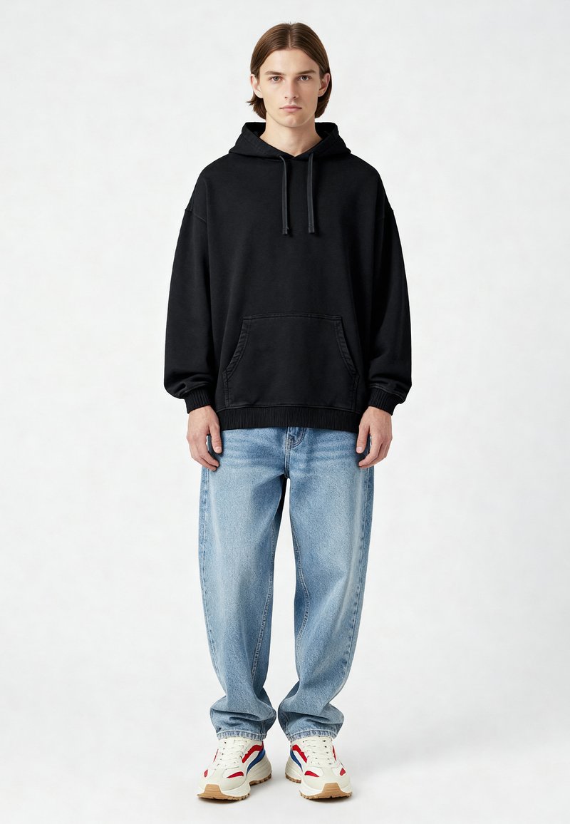 Felpa nera con cappuccio e tasca frontale, vestibilità comoda, abbinata a jeans baggy blu chiaro e sneakers multicolori con una suola testurizzata.