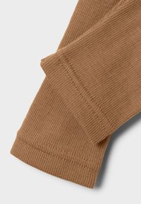 Tissu marron côtelé avec une texture lisse, présentant des bords soigneusement cousus et des poignets repliés, mettant en valeur un design doux et flexible.