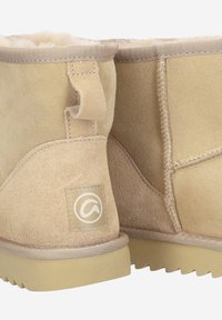 Botines de ante beige con un interior de felpa, que cuentan con una suela de goma plana, costuras en contraste y un parche con el logo en el talón.