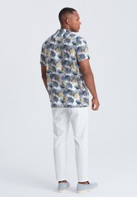 Chemise à manches courtes avec un motif coloré de feuilles et de fleurs sur un fond clair, assortie à un pantalon blanc et des chaussures grises.