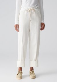 Pantalon blanc à côtes avec une coupe décontractée, doté d'une taille nouée et de poignets retroussés. Le matériau présente une apparence douce et texturée.