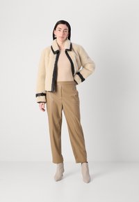 Crème schapenvachtjack met zwarte bies, lange mouwen en een kraag; gecombineerd met tan faux leren broek en beige enkellaarsjes.