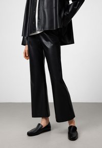 Pantaloni larghi in finta pelle nera abbinati a una camicia oversize coordinata. Scarpe slip-on nere con una finitura liscia completano il look.