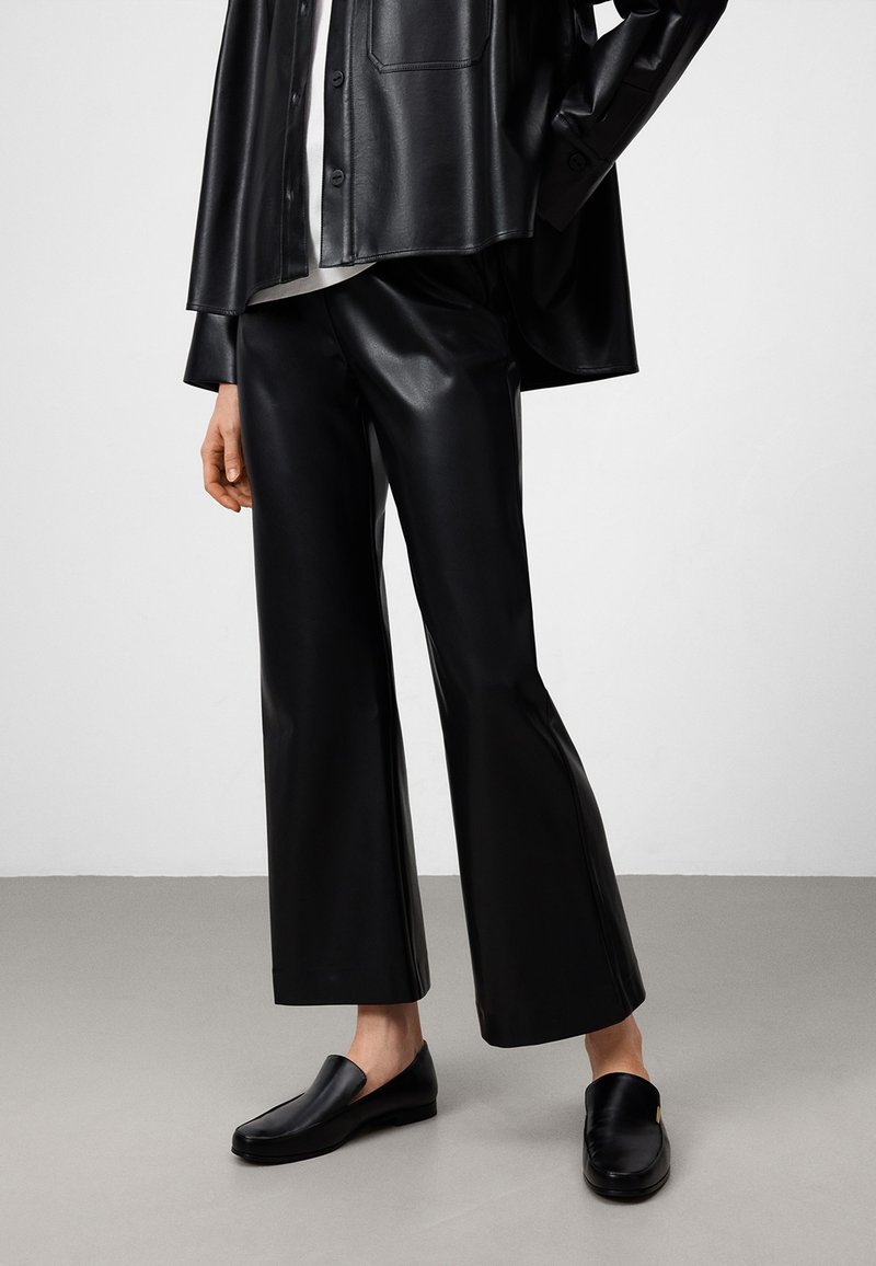 Pantaloni larghi in finta pelle nera abbinati a una camicia oversize coordinata. Scarpe slip-on nere con una finitura liscia completano il look.