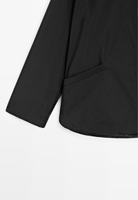 Giacca nera leggera con una texture liscia, maniche lunghe, tasche laterali e orlo curvo. Il materiale sembra essere resistente all'acqua.