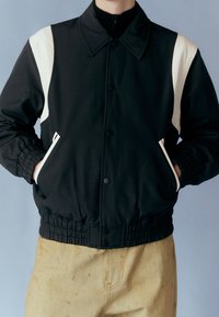 Czarna i kremowa kurtka z klasycznym kołnierzem, elastycznymi mankietami i dwoma bocznymi kieszeniami. Wykonana z gładkiej tkaniny, o luźnym kroju.