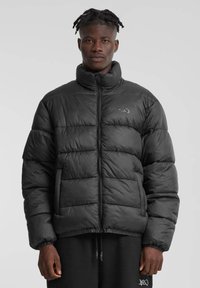 Svart puffjakke med høy krage, med glidelås og elastiske mansjetter. Designet inkluderer quiltede seksjoner for isolasjon.