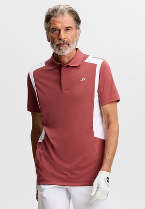 Polo rossa con pannelli laterali bianchi, maniche corte e colletto classico. Logo distintivo del marchio sul petto. Indossata con pantaloni bianchi e guanto da golf.