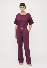 Paarse t-shirt met korte mouwen en een ronde hals, gecombineerd met bijpassende elastische broek, beide in een gladde, matte stof.