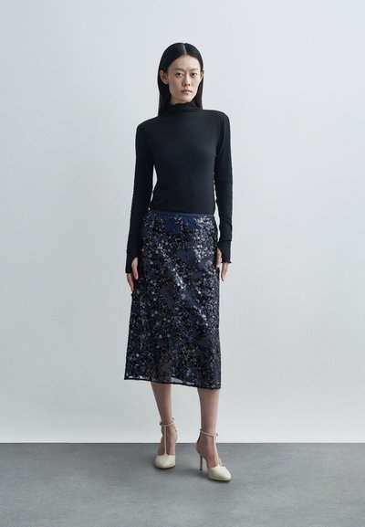 Black long-sleeve top with ribbed texture; navy floral-patterned midi skirt; beige high-heeled shoes with ankle straps.
