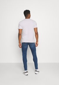 Camiseta de manga corta color gris claro combinada con vaqueros ajustados de color azul oscuro, con una textura sutil y un cuello redondo estándar. Zapatillas completan el conjunto.