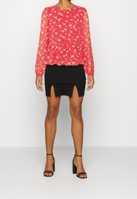 Top lungo a maniche con stampa floreale rossa e orlo peplum abbinato a una mini gonna nera con spacchi frontali e sandali neri con tacco alto.