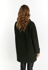 Mørkegrønt oversized jakke med tekstureret stof, flad krave, lange ærmer og sænket skuldre, parret med sorte læderbukser.