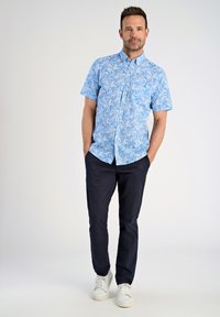 Korte mouwen, lichtblauw overhemdd met een bloemenpatroon, gecombineerd met donkere broeken en witte sneakers. Gladde stof en een getailleerde pasvorm.