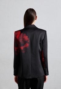Schwarze Blazer mit großem rotem Blumenmuster auf der linken Schulter und dem Rücken, satinierte Textur, Ein-Knopf-Front und sechs-Knopf-Manschetten.