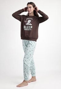 Sudadera marrón con gráfico de "Snoopy Sleep Society" y pantalones de pijama azul claro con un patrón de pingüinos. Tejido suave, ajuste relajado.