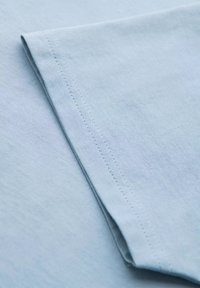 Světle modrá bavlněná látka s hladkou texturou, s přeloženým rukávem a úhledným švem, který zdůrazňuje její jemný a jednoduchý design.