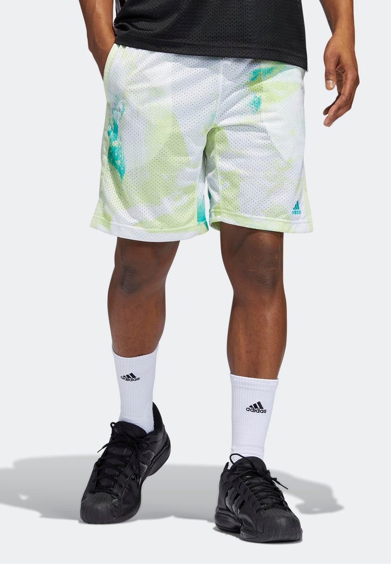 Bermudas deportivas de malla blanca con patrones abstractos en verde y azul, con una cintura elástica. Combinadas con zapatillas negras y calcetines blancos.