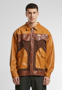 Braune und beige Jacke aus einer Mischung aus Leder und Cord, mit einem Kragen, Druckknöpfen und zwei großen Fronttaschen.