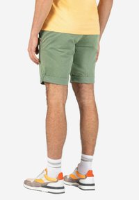 Grüne Baumwollshorts mit umgeschlagenen Säumen, kombiniert mit weißen Socken und mehrfarbigen Turnschuhen. Einfaches Design mit einer seitlichen Taschenraffung.